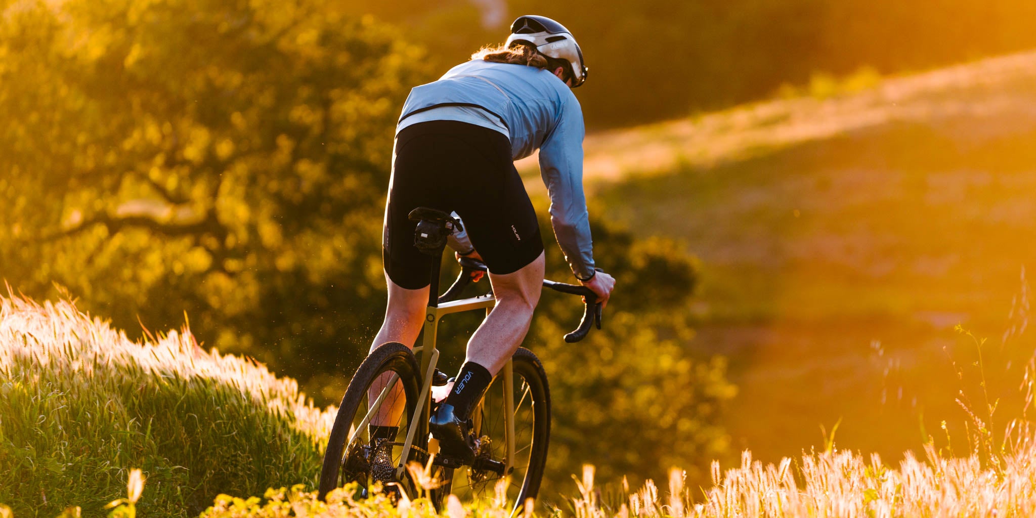 golden hour cyclist from behind on trail riding a gravel bike in jacket and black label bibs