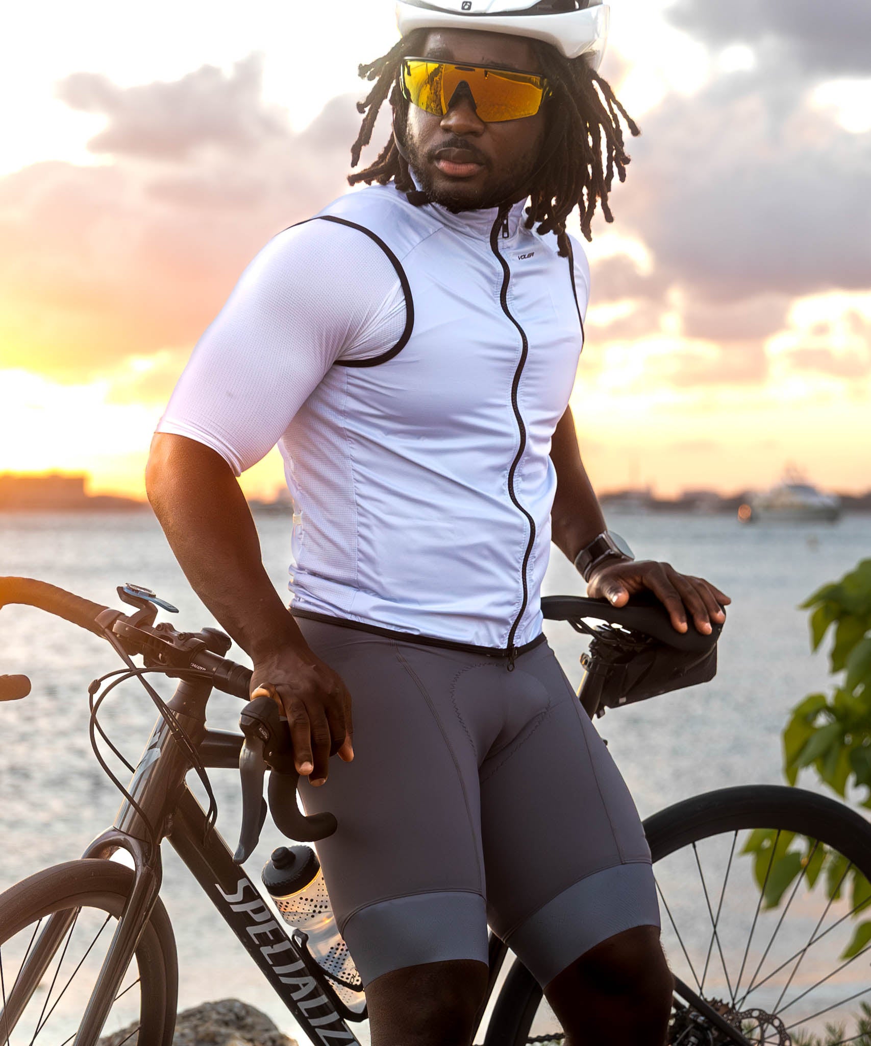 Man in cycling gear with a bicycle by a waterfront at sunset