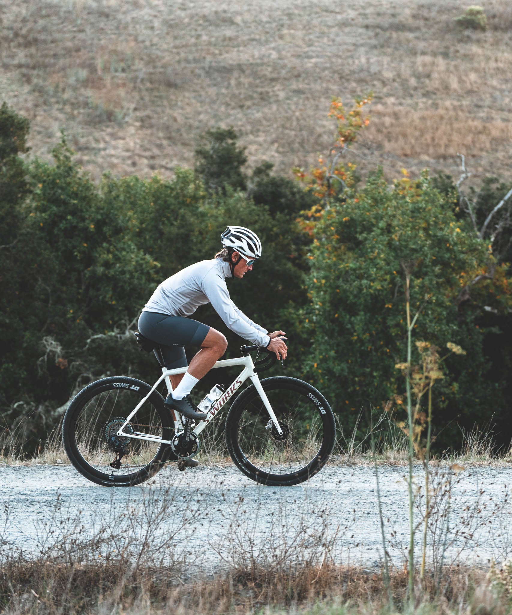 Person riding a bicycle on a rural road with trees and open fields in the background