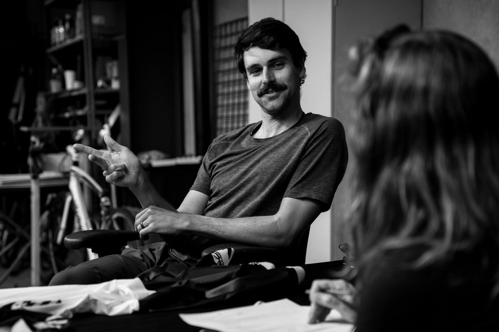 Two people talking beside garments on a worktable at Voler.