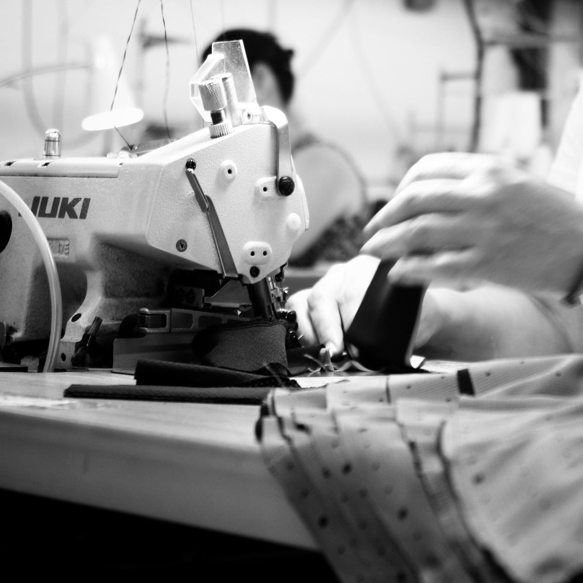 Black-and-white close-up of fabric being guided through a sewing machine at Voler.